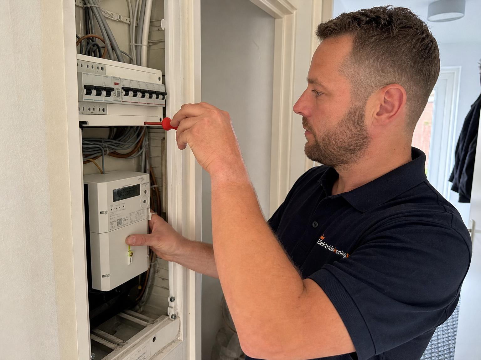 Nederlandse elektricien in donker werkshirt en zwarte werkbroek voor een bakstenen rijtjeshuis